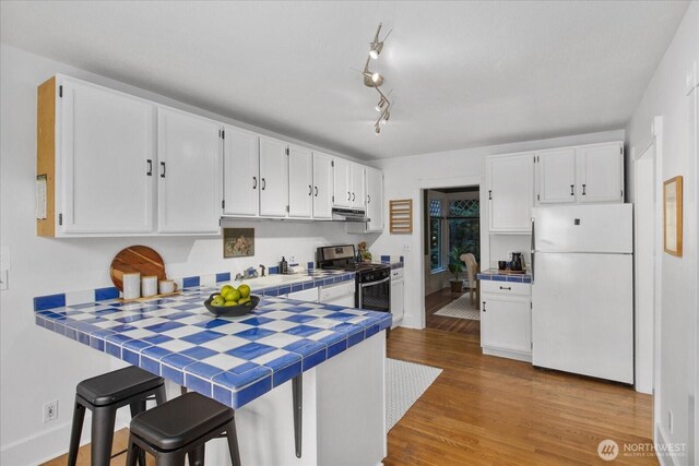 5825 4th Ave NW, Seattle, WA 98107 - kitchen with freestanding refrigerator, tile countertops, stainless steel range with gas stovetop, white cabinets, and a peninsula