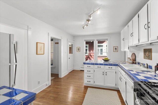 5825 4th Ave NW, Seattle, WA 98107 - kitchen with freestanding refrigerator, tile countertops, white cabinets, wood finished floors, and a baseboard heating unit