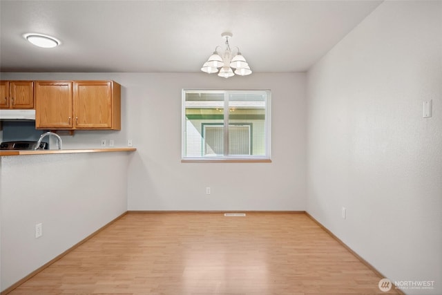 1726 Ann St NE, Olympia, WA 98506 - kitchen with under cabinet range hood, light wood finished floors, a chandelier, pendant lighting, and brown cabinetry