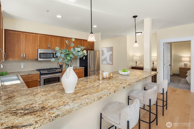 1840 25th Ave NE Unit 210, Issaquah, WA 98029 - kitchen featuring appliances with stainless steel finishes, brown cabinetry, light wood-style flooring, tasteful backsplash, and a kitchen bar