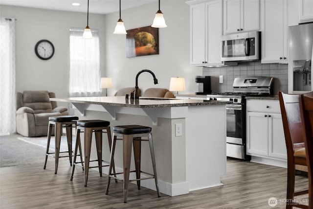 397 N Foster St, Buckley, WA 98321 - kitchen featuring stainless steel appliances, wood finished floors, a breakfast bar area, a kitchen island with sink, and decorative backsplash