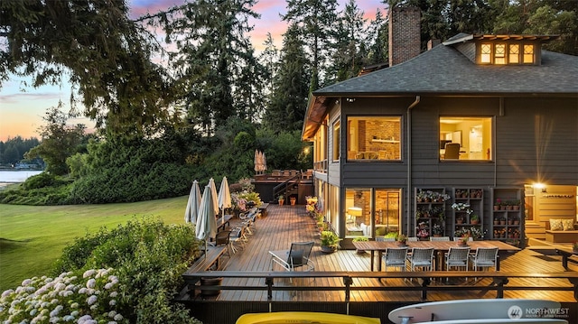 5222 Mahncke Rd SW, Longbranch, WA 98351 - back of house at dusk with a deck, a lawn, a chimney, a shingled roof, and outdoor dining space