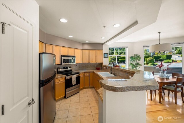 2244 SE 132nd Ave Unit B217, Bellevue, WA 98005 - kitchen featuring appliances with stainless steel finishes, a peninsula, tile counters, light brown cabinetry, and backsplash