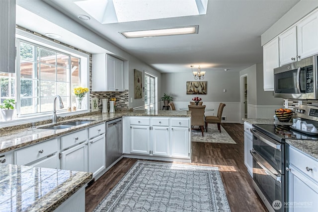 18920 217th Ave E, Orting, WA 98360 - kitchen with appliances with stainless steel finishes, a peninsula, a skylight, dark wood-style flooring, and white cabinetry
