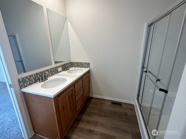 2101 S 324th St Unit 228, Federal Way, WA 98003 - bathroom featuring double vanity, wood finished floors, decorative backsplash, and a shower with door