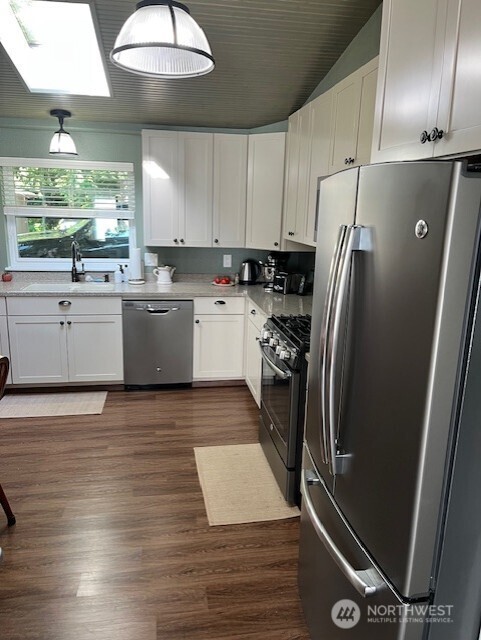 20011 Tveit Rd, Arlington, WA 98223 - kitchen featuring appliances with stainless steel finishes, white cabinetry, dark wood finished floors, light countertops, and a skylight