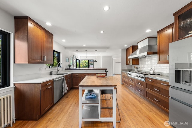 3516 NE 43rd St, Seattle, WA 98105 - kitchen with appliances with stainless steel finishes, radiator heating unit, a peninsula, wall chimney range hood, and light wood-type flooring