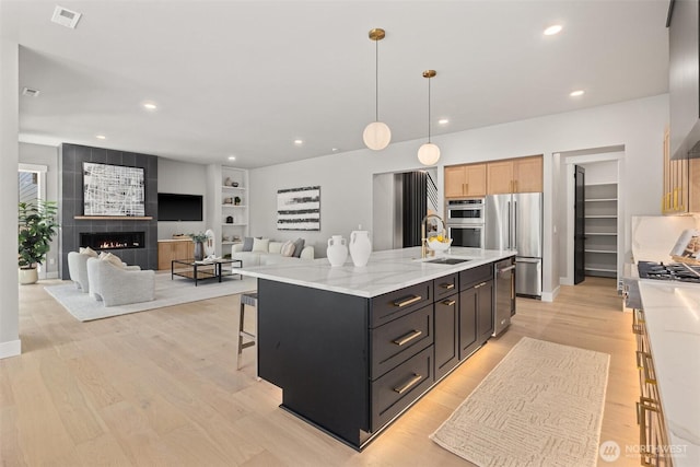 16429 Snohomish Ave SE, Clearview, WA 98296 - kitchen with stainless steel appliances, a tiled fireplace, light wood-style flooring, an island with sink, and decorative light fixtures