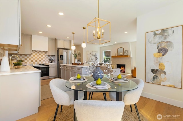3430 42nd Ave SW, Seattle, WA 98116 - dining space with light wood-type flooring, a chandelier, a lit fireplace, and recessed lighting