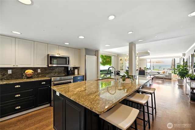 9717 NE Juanita Dr Unit 101, Kirkland, WA 98034 - kitchen with stainless steel microwave, stove, paneled refrigerator, dark cabinetry, and wood finished floors