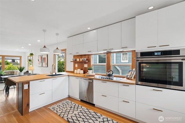 3211 16th Ave S, Seattle, WA 98144 - kitchen with stainless steel appliances, a peninsula, light wood-style floors, white cabinets, and wood counters