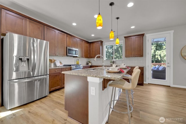 11103 5th Ave SW, Seattle, WA 98146 - kitchen with stainless steel appliances, light wood finished floors, light stone countertops, decorative backsplash, and decorative light fixtures