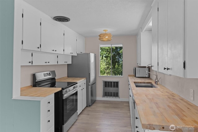 1173 Grauel Ramapo Rd, Port Angeles, WA 98363 - kitchen featuring appliances with stainless steel finishes, light wood-type flooring, white cabinets, a textured ceiling, and wood counters