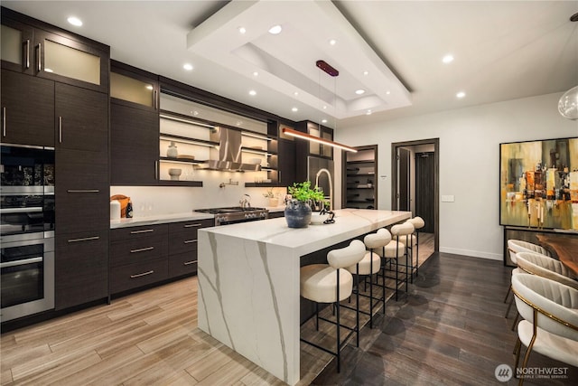 11210 SE 74th St, Newcastle, WA 98056 - kitchen featuring island range hood, recessed lighting, a tray ceiling, a kitchen bar, and light wood finished floors