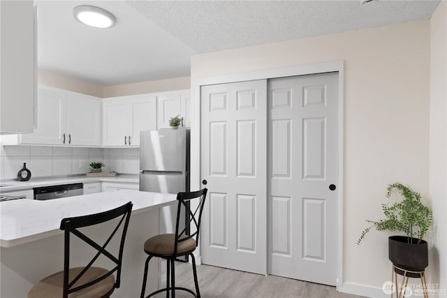 13838 NE 60th St Unit 165, Redmond, WA 98052 - kitchen featuring appliances with stainless steel finishes, a kitchen bar, white cabinets, light wood-style flooring, and tasteful backsplash