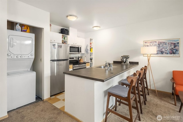 1610 Belmont Ave Unit 314, Seattle, WA 98122 - kitchen with stainless steel appliances, stacked washer / dryer, a peninsula, dark countertops, and white cabinetry