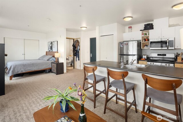 1610 Belmont Ave Unit 314, Seattle, WA 98122 - kitchen featuring stainless steel appliances, a breakfast bar area, dark countertops, white cabinetry, and light carpet