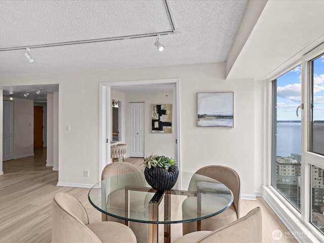 121 Vine St Unit 2405, Seattle, WA 98121 - dining room with rail lighting, light wood-type flooring, a textured ceiling, and a water view