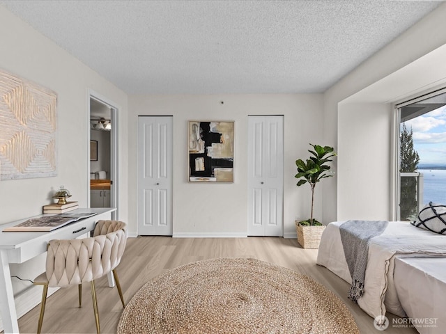 121 Vine St Unit 2405, Seattle, WA 98121 - bedroom featuring multiple closets, light wood finished floors, a textured ceiling, a desk, and connected bathroom