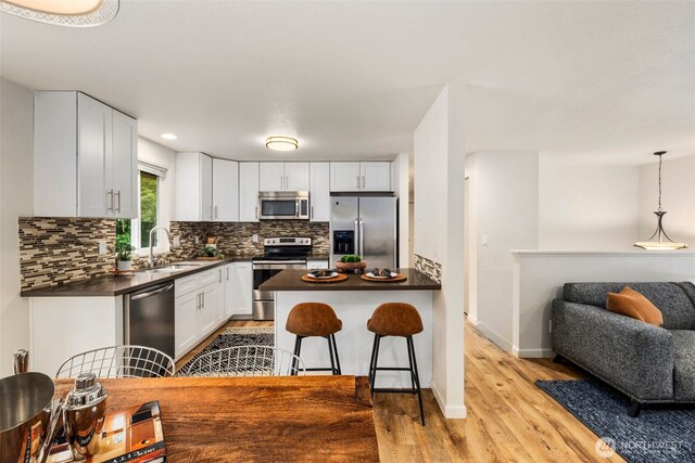 4133 23rd Ave SW, Seattle, WA 98106 - kitchen with appliances with stainless steel finishes, dark countertops, light wood-type flooring, tasteful backsplash, and white cabinetry