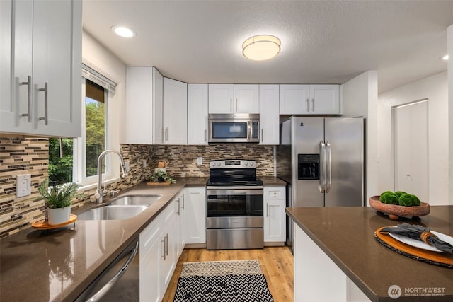 4133 23rd Ave SW, Seattle, WA 98106 - kitchen with stainless steel appliances, light wood finished floors, white cabinets, decorative backsplash, and dark stone counters