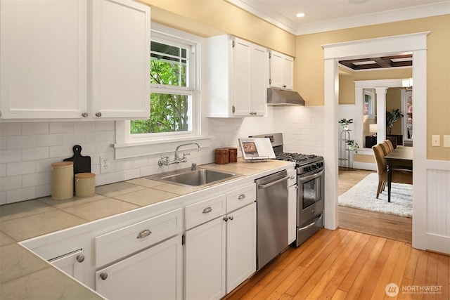 4010 Interlake Ave N, Seattle, WA 98103 - kitchen with ornamental molding, appliances with stainless steel finishes, under cabinet range hood, white cabinetry, and light wood-style floors