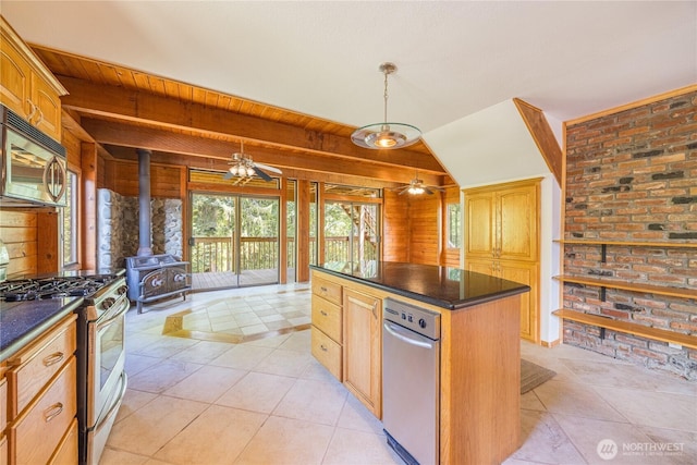 71 Waggler Way, Sequim, WA 98382 - kitchen with appliances with stainless steel finishes, a wood stove, dark countertops, a ceiling fan, and a kitchen island