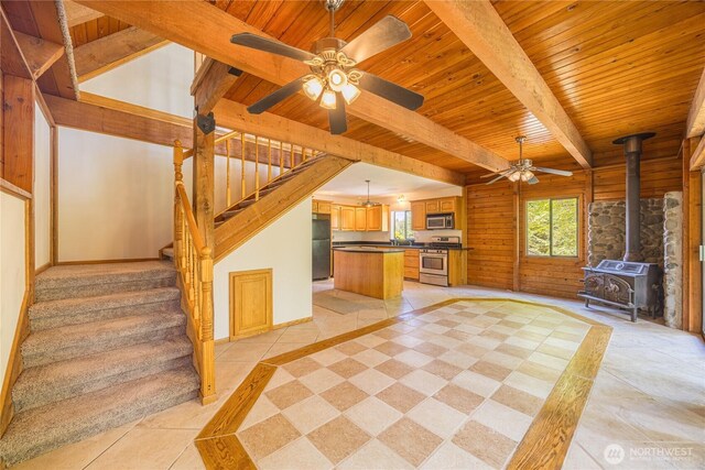 71 Waggler Way, Sequim, WA 98382 - unfurnished living room featuring a wooden ceiling with exposed beams, ceiling fan, a wood stove, stairs, and light tile patterned floors