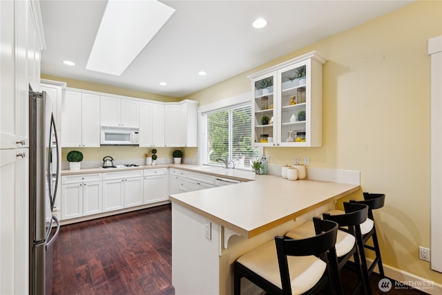 2218 Cascade Ct, Anacortes, WA 98221 - kitchen featuring white appliances, a peninsula, dark wood-type flooring, white cabinetry, and a kitchen bar