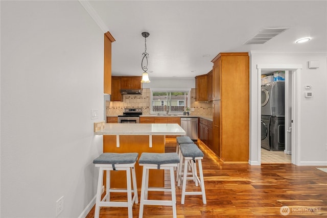 4248 A St SE Unit 423, Auburn, WA 98002 - kitchen featuring appliances with stainless steel finishes, a peninsula, stacked washer and clothes dryer, wood finished floors, and brown cabinets
