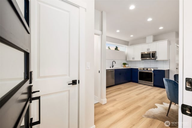 9692 51st Ave S, Seattle, WA 98118 - kitchen with stainless steel appliances, blue cabinetry, tasteful backsplash, light countertops, and light wood-type flooring