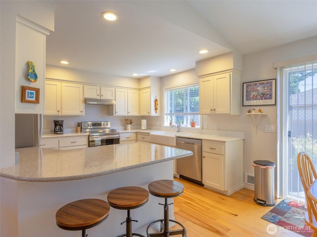 501 Summer Breeze Ln, Sequim, WA 98382 - kitchen featuring stainless steel appliances, under cabinet range hood, light wood-type flooring, a kitchen bar, and white cabinets