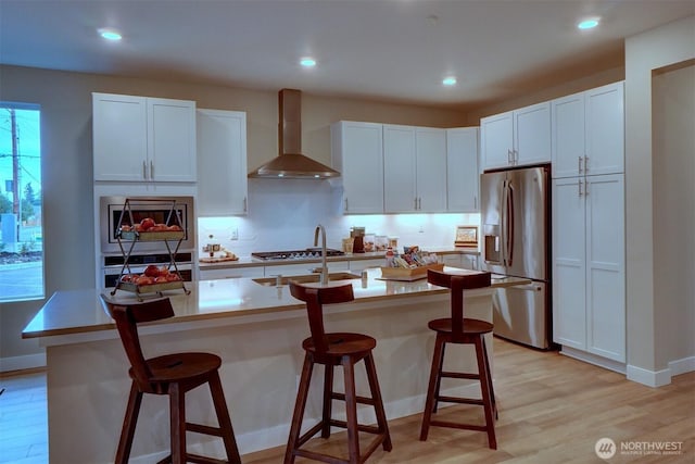29207 217th Pl SE Unit 1, Black Diamond, WA 98010 - kitchen with stainless steel appliances, wall chimney exhaust hood, light wood-style floors, backsplash, and a kitchen breakfast bar