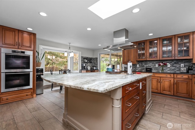 4709 144th St E, Tacoma, WA 98446 - kitchen with island range hood, stainless steel double oven, recessed lighting, brown cabinetry, and light stone countertops