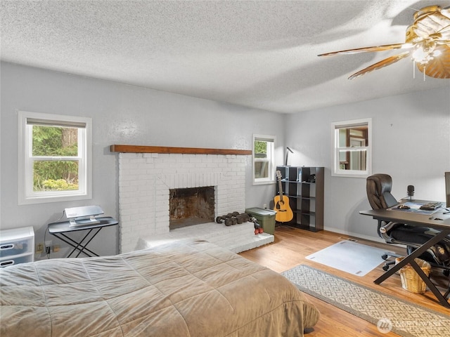 6908 254th St E, Graham, WA 98338 - bedroom with wood finished floors, multiple windows, a textured ceiling, a fireplace, and an office area
