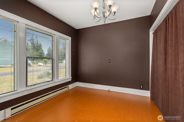 802 May St, Raymond, WA 98577 - empty room with baseboard heating, a chandelier, plenty of natural light, and wood finished floors
