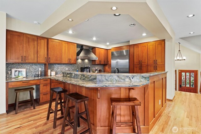 18608 SE 58th St, Issaquah, WA 98027 - kitchen with built in refrigerator, wall chimney range hood, light wood finished floors, tasteful backsplash, and brown cabinets
