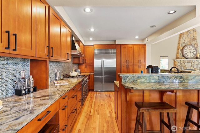 18608 SE 58th St, Issaquah, WA 98027 - kitchen featuring premium appliances, wall chimney range hood, a kitchen breakfast bar, light wood-style floors, and brown cabinetry