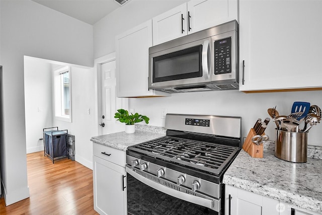 807 24th St, Anacortes, WA 98221 - kitchen with stainless steel appliances, white cabinets, light wood-type flooring, and light stone counters