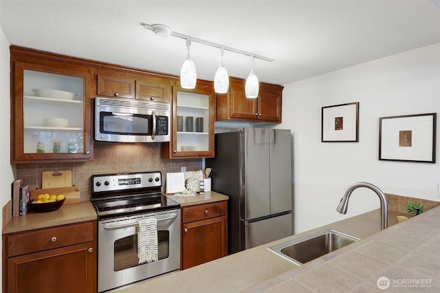 300 N 130th St Unit 2306, Seattle, WA 98133 - kitchen with appliances with stainless steel finishes, light countertops, hanging light fixtures, glass insert cabinets, and brown cabinetry