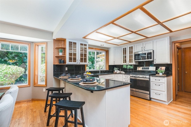 2327 31st Ave NW, Olympia, WA 98502 - kitchen with stainless steel appliances, a peninsula, glass insert cabinets, a kitchen bar, and decorative backsplash
