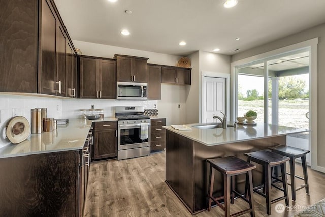 28003 74th Ave NW Unit 33, Stanwood, WA 98292 - kitchen with appliances with stainless steel finishes, dark brown cabinetry, light wood-type flooring, a kitchen bar, and recessed lighting