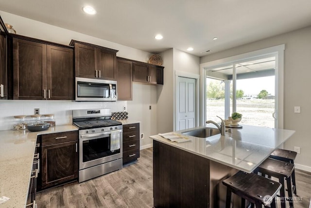 28003 74th Ave NW Unit 33, Stanwood, WA 98292 - kitchen featuring stainless steel appliances, light wood finished floors, dark brown cabinetry, light stone countertops, and a breakfast bar area