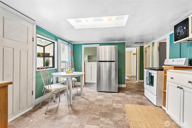1814 Wilson Ave, Bellingham, WA 98225 - kitchen with freestanding refrigerator, white range with electric stovetop, a skylight, white cabinets, and stone finish flooring