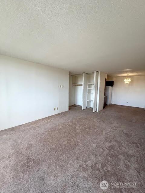 4540 8th Ave NE Unit 903, Seattle, WA 98105 - unfurnished living room featuring carpet, a textured ceiling, and a chandelier