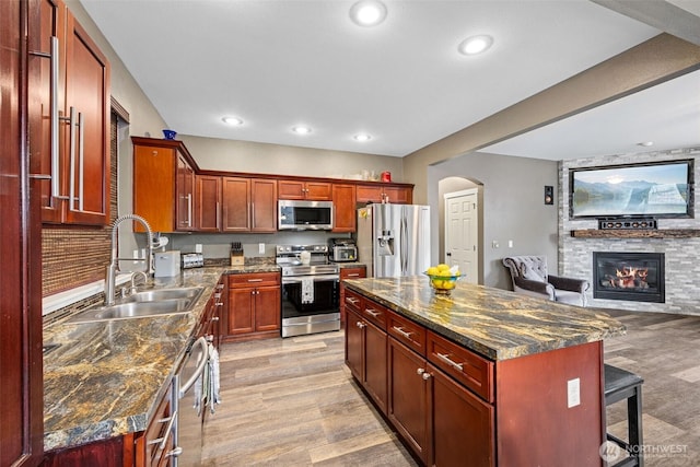 7726 162nd St E, Puyallup, WA 98375 - kitchen with appliances with stainless steel finishes, arched walkways, light wood finished floors, open floor plan, and a stone fireplace