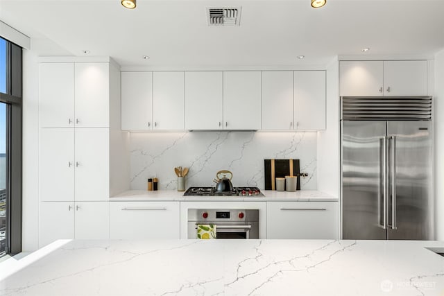 2033 2nd Ave Unit 1111, Seattle, WA 98121 - kitchen with stainless steel appliances, light stone countertops, white cabinetry, recessed lighting, and decorative backsplash