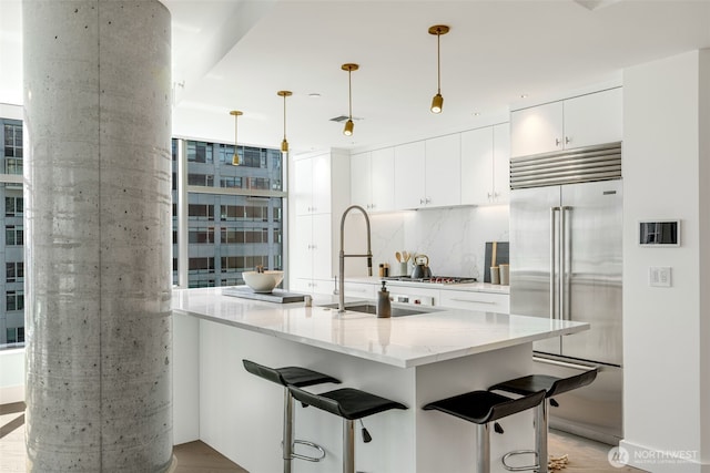 2033 2nd Ave Unit 1111, Seattle, WA 98121 - kitchen featuring built in refrigerator, white cabinetry, a breakfast bar area, light stone counters, and decorative light fixtures
