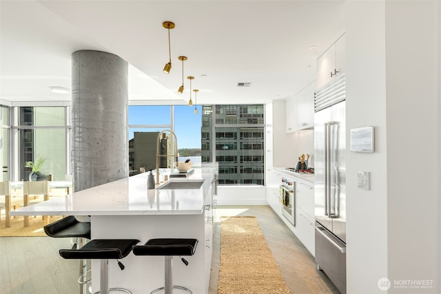 2033 2nd Ave Unit 1111, Seattle, WA 98121 - kitchen featuring stainless steel appliances, light wood-style floors, white cabinets, decorative light fixtures, and a center island with sink