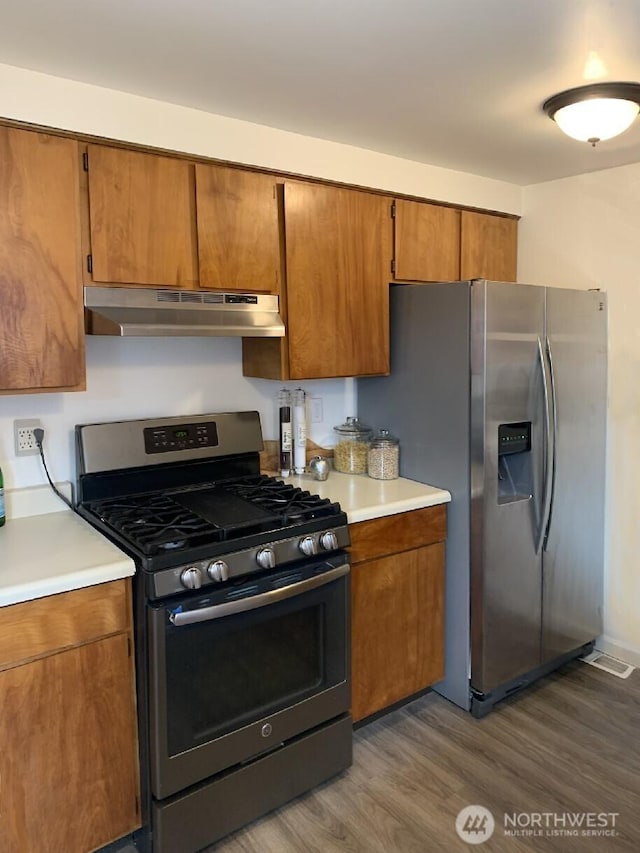 5910 21st Ave SW, Seattle, WA 98106 - kitchen featuring appliances with stainless steel finishes, under cabinet range hood, brown cabinets, dark wood-style floors, and light countertops